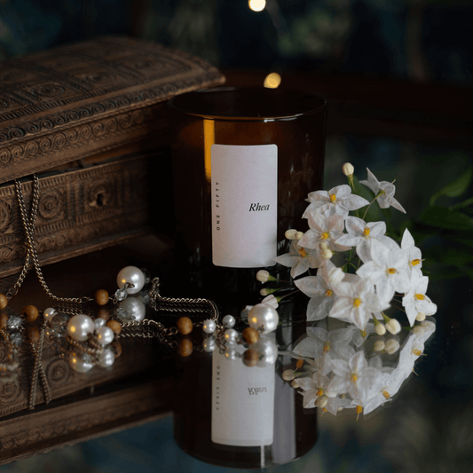 A glass amber candle vessel against an aged jewellery box with pearls and natural flowers 