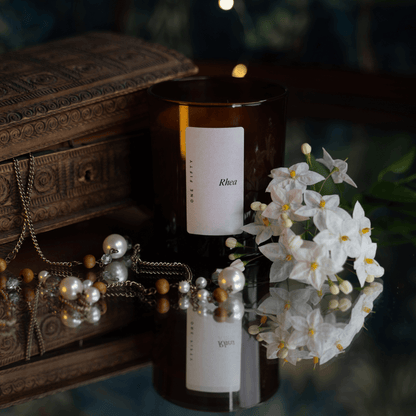 A glass amber candle vessel against an aged jewellery box with pearls and natural flowers 